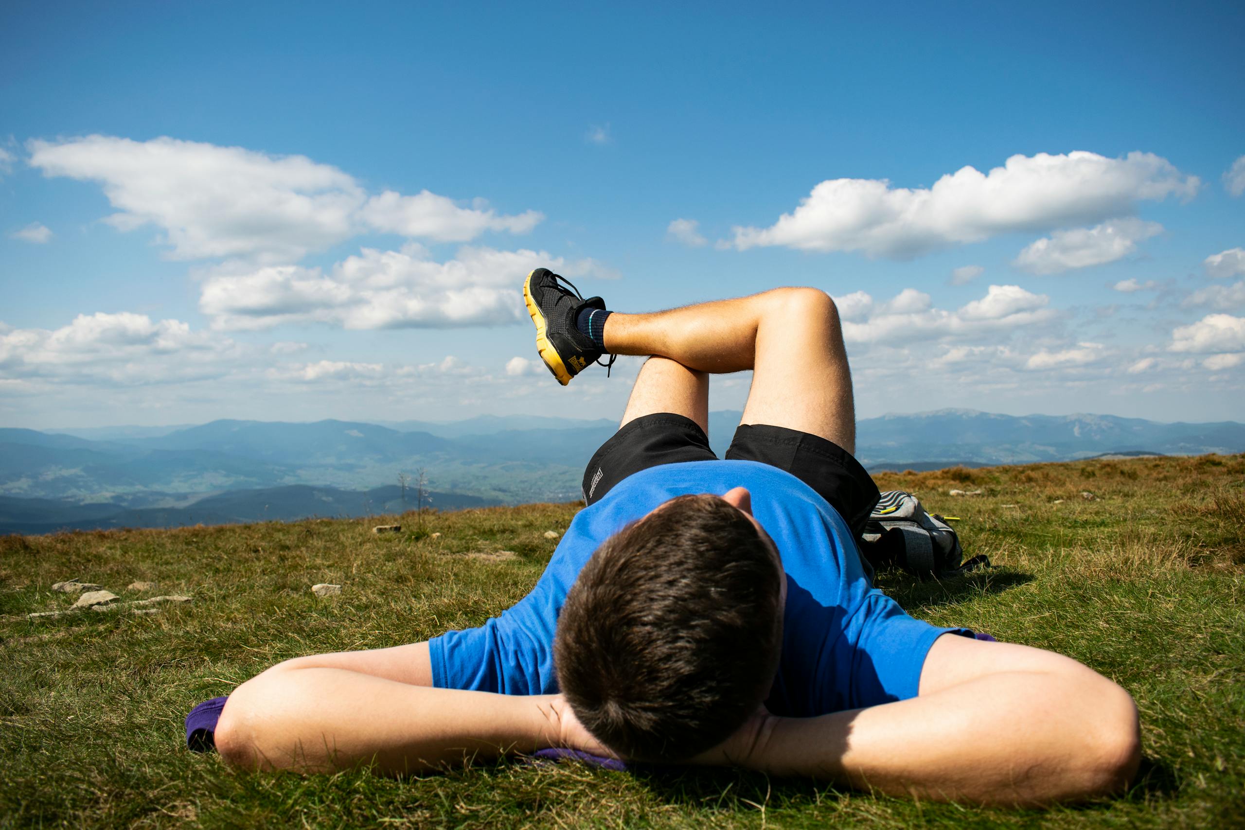 Unrecognizable young male athlete in sportswear lying on grassy ground in mountainous terrain and resting after outdoor workout